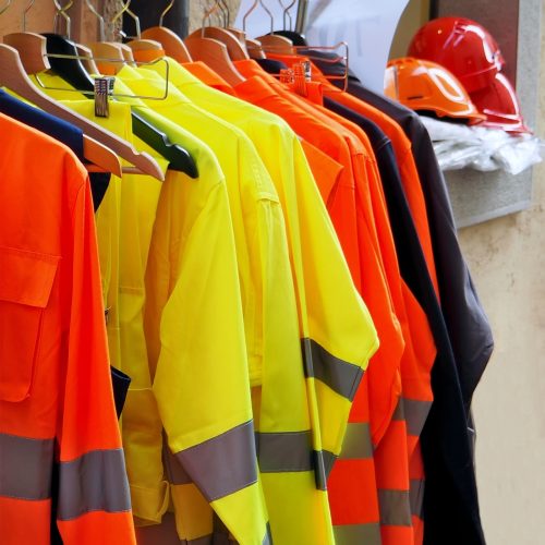 High visibility jackets on a hanger with protective helmets behind, in a work clothes store .